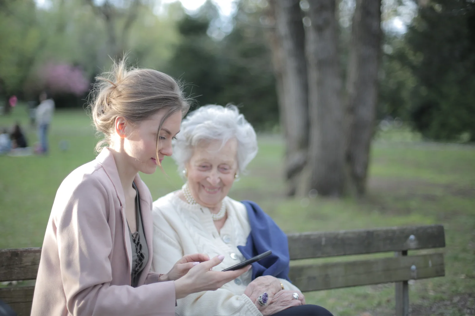Granddaughter showing her grandmother a phone on a park bench